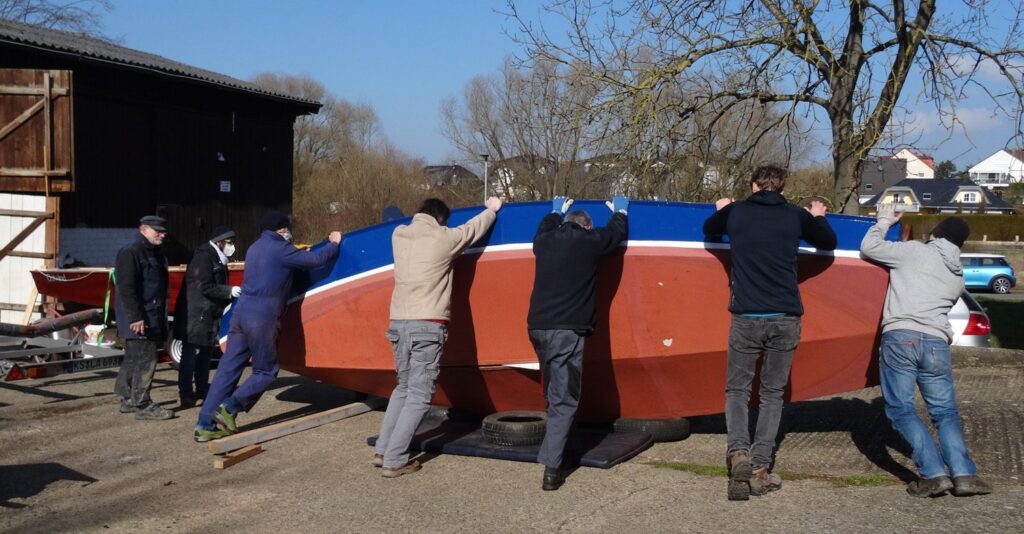 Die erste Wende in 2022. Die Bootsarbeiten haben begonnen. Die Jollen werden mit versammelten Kräften vom Trailer gehoben und Kieloben gelegt, um das Unterwasserschiff bearbeiten zu können – Das muntere Jollendrehen komplett als Slideshow unter "Eindrücke/Galereien"