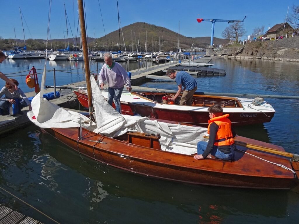 Die Traditionsjollen aus Holz. Bei der Lightning wird das Stellen des Mastes vorbereitet. Der Prirat legt wieder an nach einer ersten Runde unter Segeln